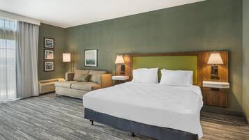 A hotel room with a large bed, a sofa, two bedside lamps, a wall-mounted TV, and a window with curtains.