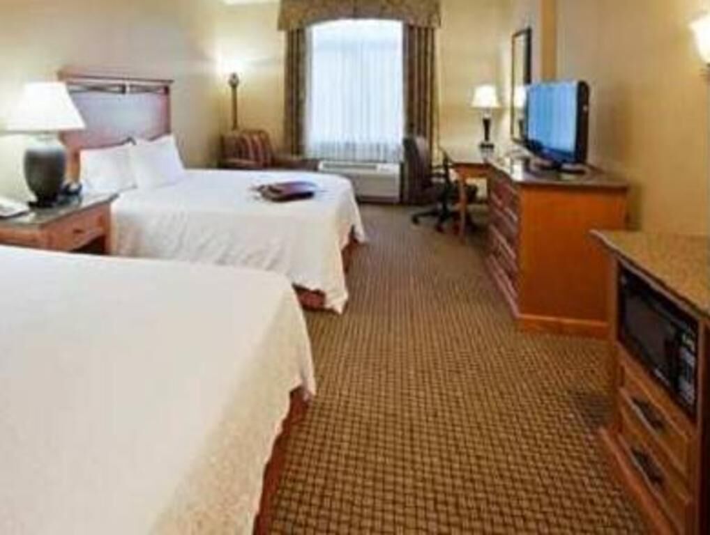 Een hotelkamer met twee bedden, een bureau, een televisie en een raam met gordijnen.
