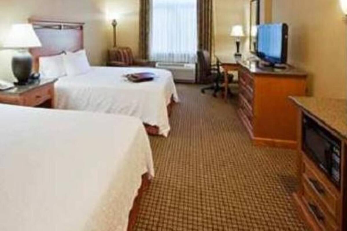 A hotel room with two beds, a desk, a television, and a window with curtains.