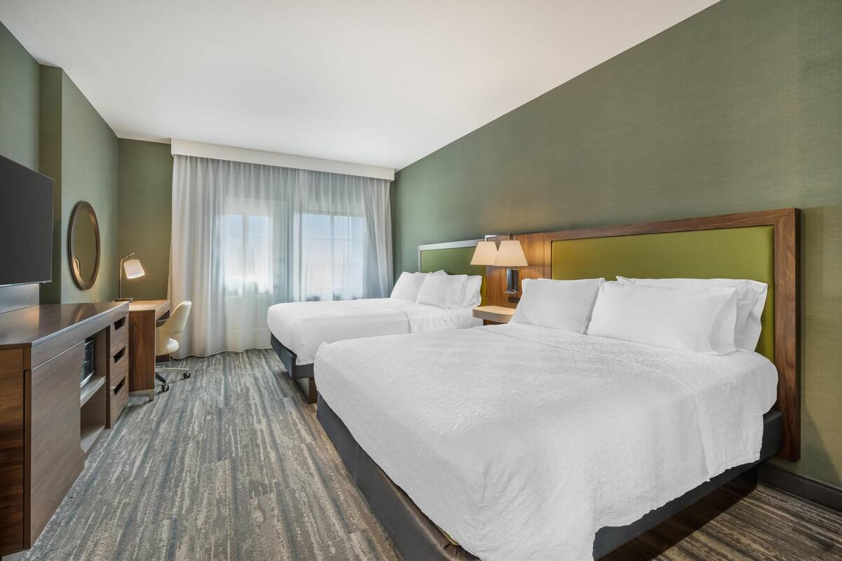 Habitación de hotel con dos camas, un escritorio, una silla, un televisor y una ventana con cortinas.