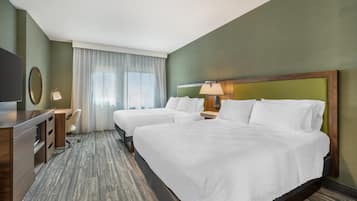 A hotel room with two beds, a desk, a chair, a TV, and a window with curtains.