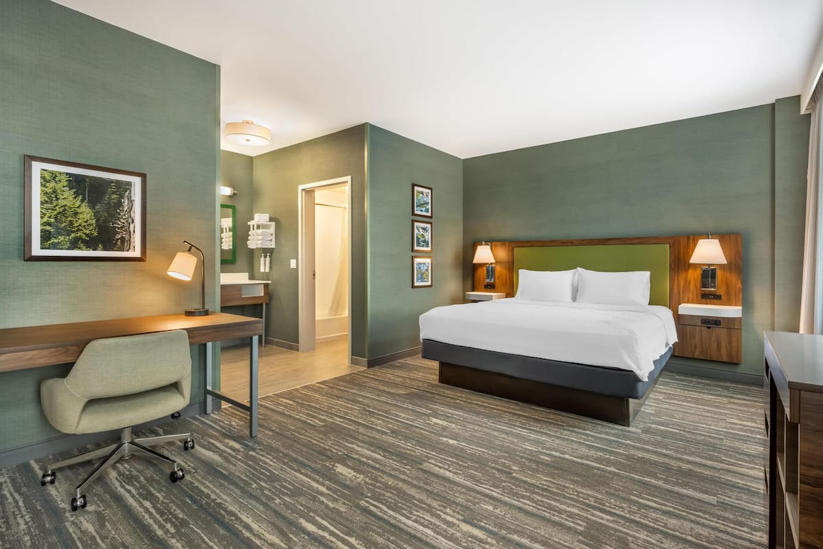 Habitación de hotel con cama, escritorio, silla y dos lámparas de noche.