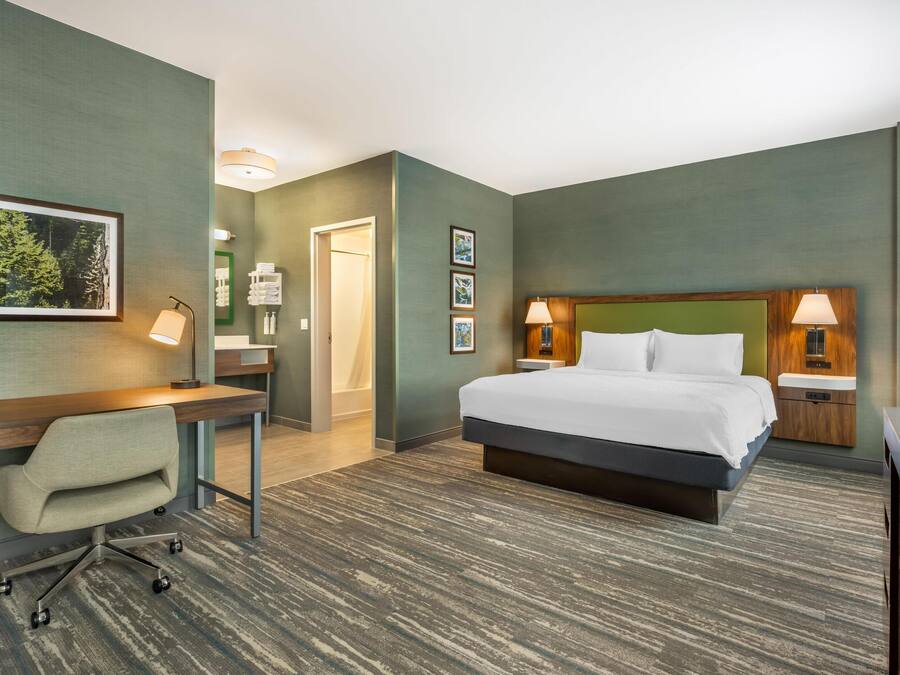A hotel room with a bed, desk, chair, and two bedside lamps.