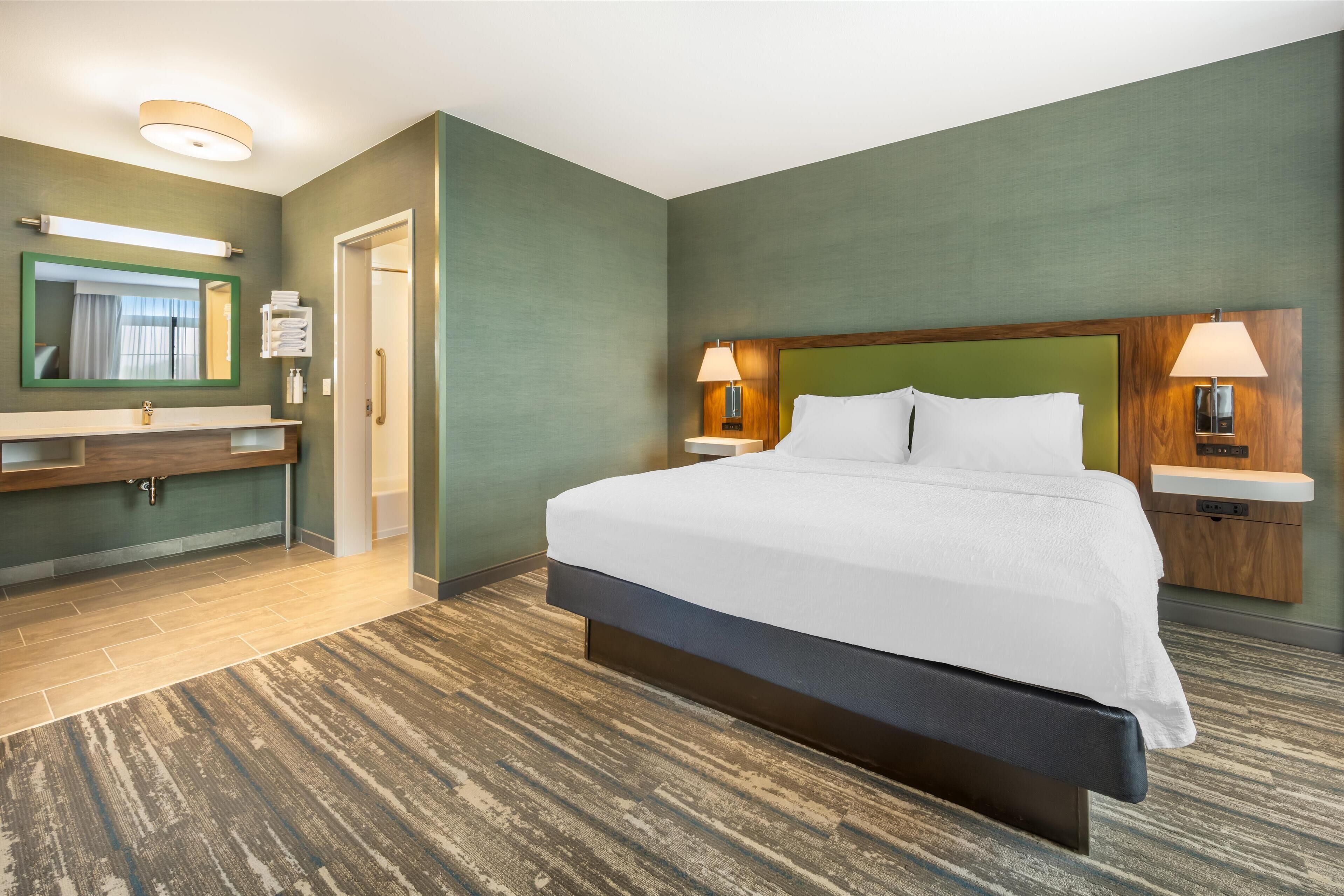 A hotel room with a large bed, a vanity with a mirror, and two bedside lamps.