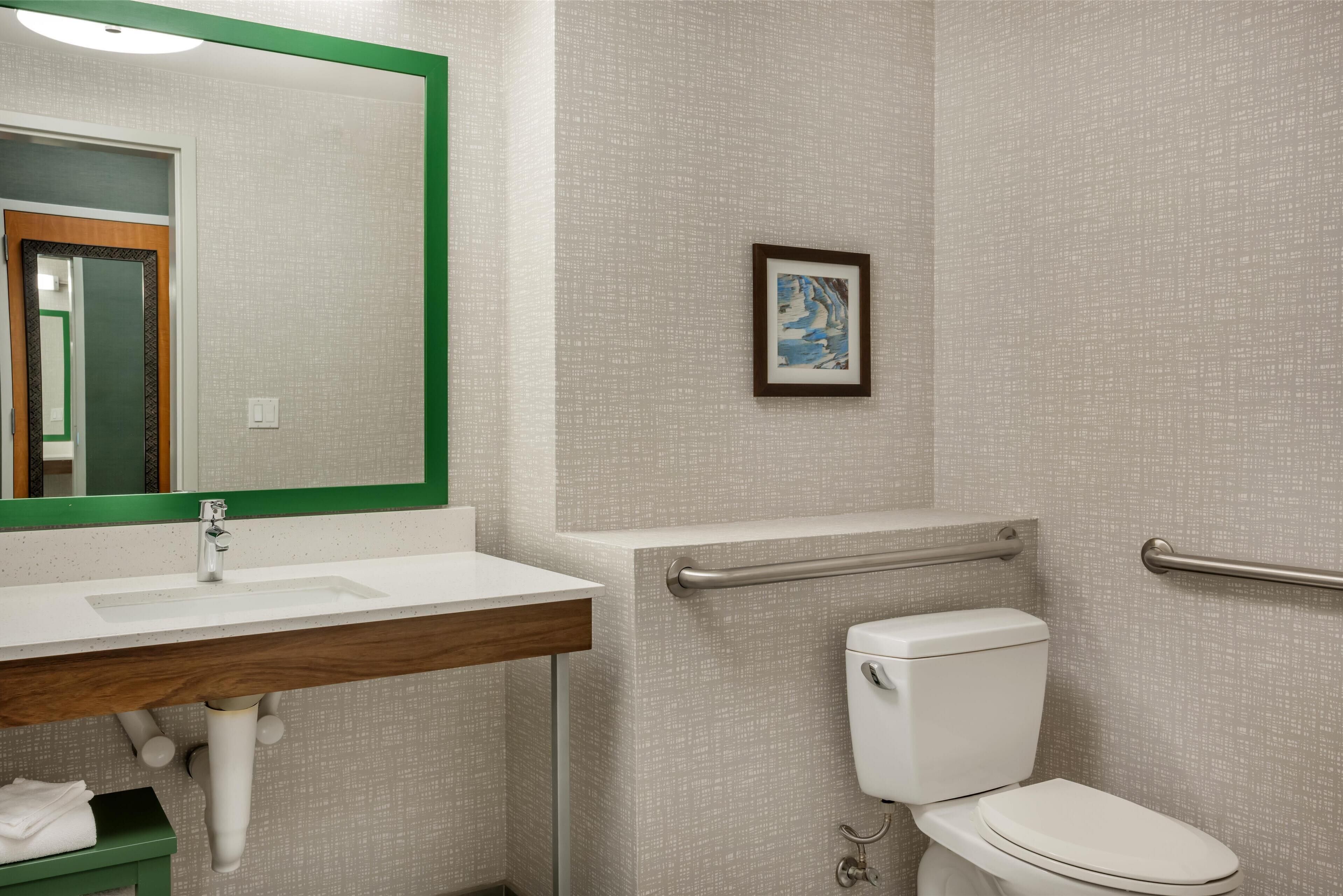 A bathroom with a white sink, mirror, toilet, and handrails.