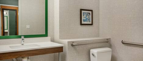 A bathroom with a white sink, mirror, toilet, and handrails.