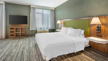 Une chambre d’hôtel avec un grand lit, une télévision, un bureau et une fenêtre avec des rideaux.
