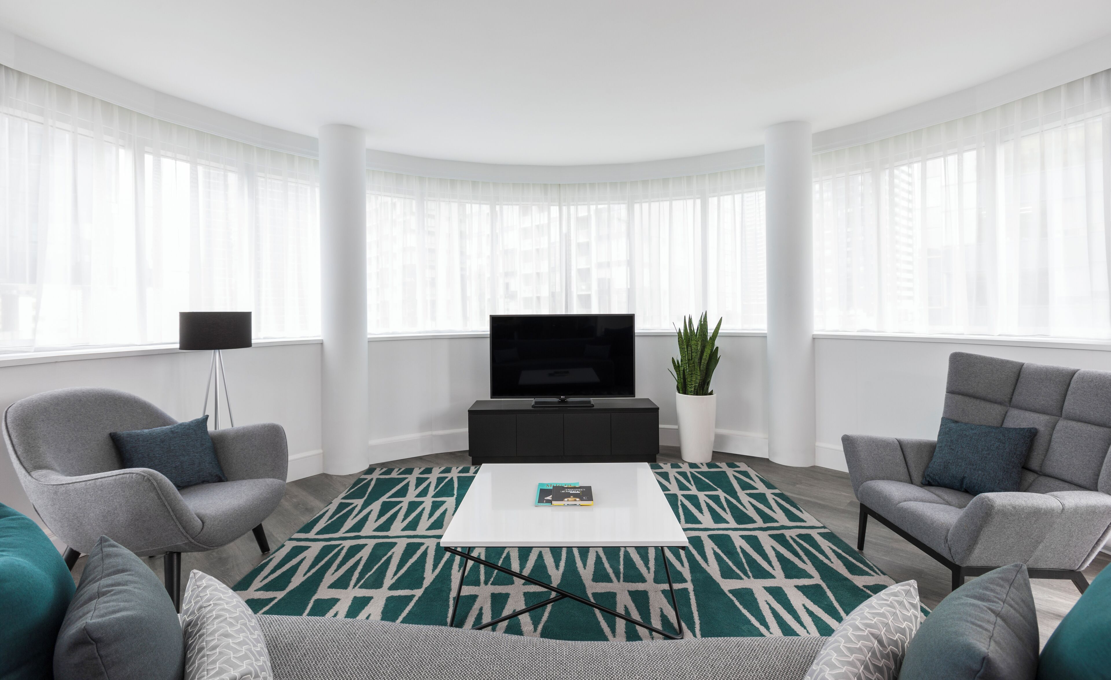 A modern living room with a flat-screen TV, two grey armchairs, a coffee table, and a patterned rug.
