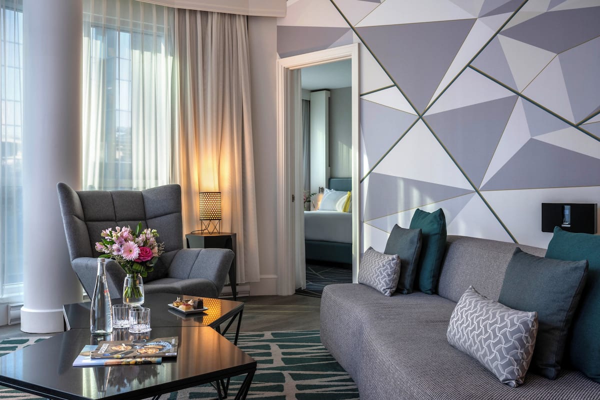 Una habitación de hotel moderna con un sofá, un sillón y una mesa de centro con una revista.