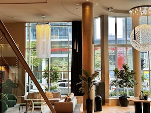 A modern lobby with a staircase, seating area, large windows, and a decorative chandelier. - Warwick Le Crystal - Montréal (Montreal)