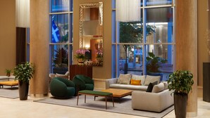Eine geräumige Lobby mit großen Fenstern, einer Sitzecke mit Sofas und Sesseln sowie dekorativen Pflanzen.