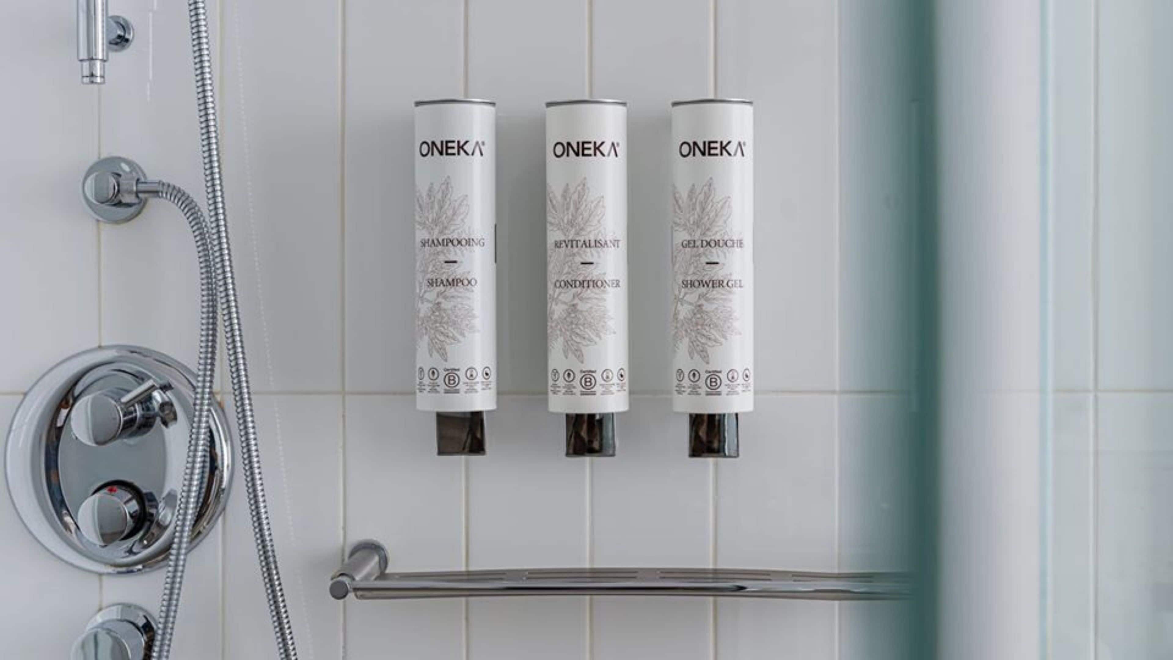 A bathroom with a shower, a handheld showerhead, and three Oneka product dispensers for shampoo, conditioner, and shower gel.