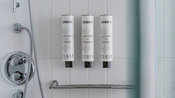 A bathroom with a shower, a handheld showerhead, and three Oneka product dispensers for shampoo, conditioner, and shower gel.