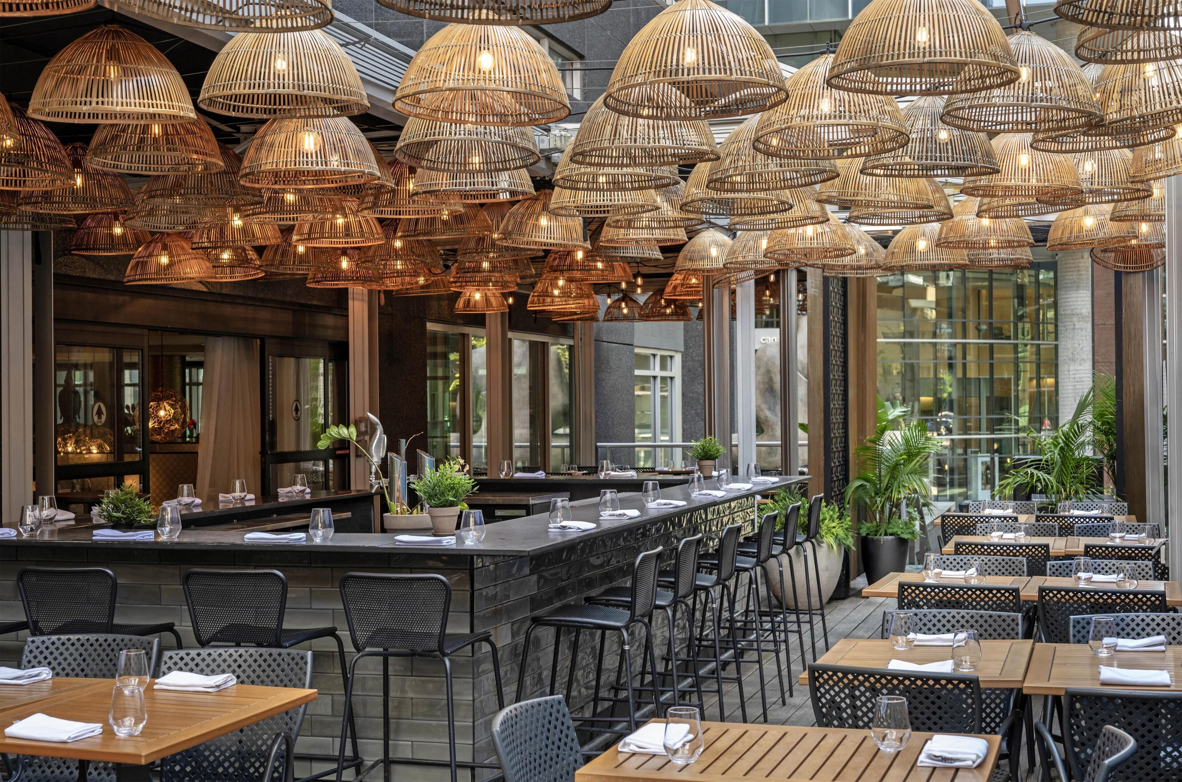 Un restaurant doté d’un long bar, de nombreuses tables et de lampes en osier suspendues au plafond.
