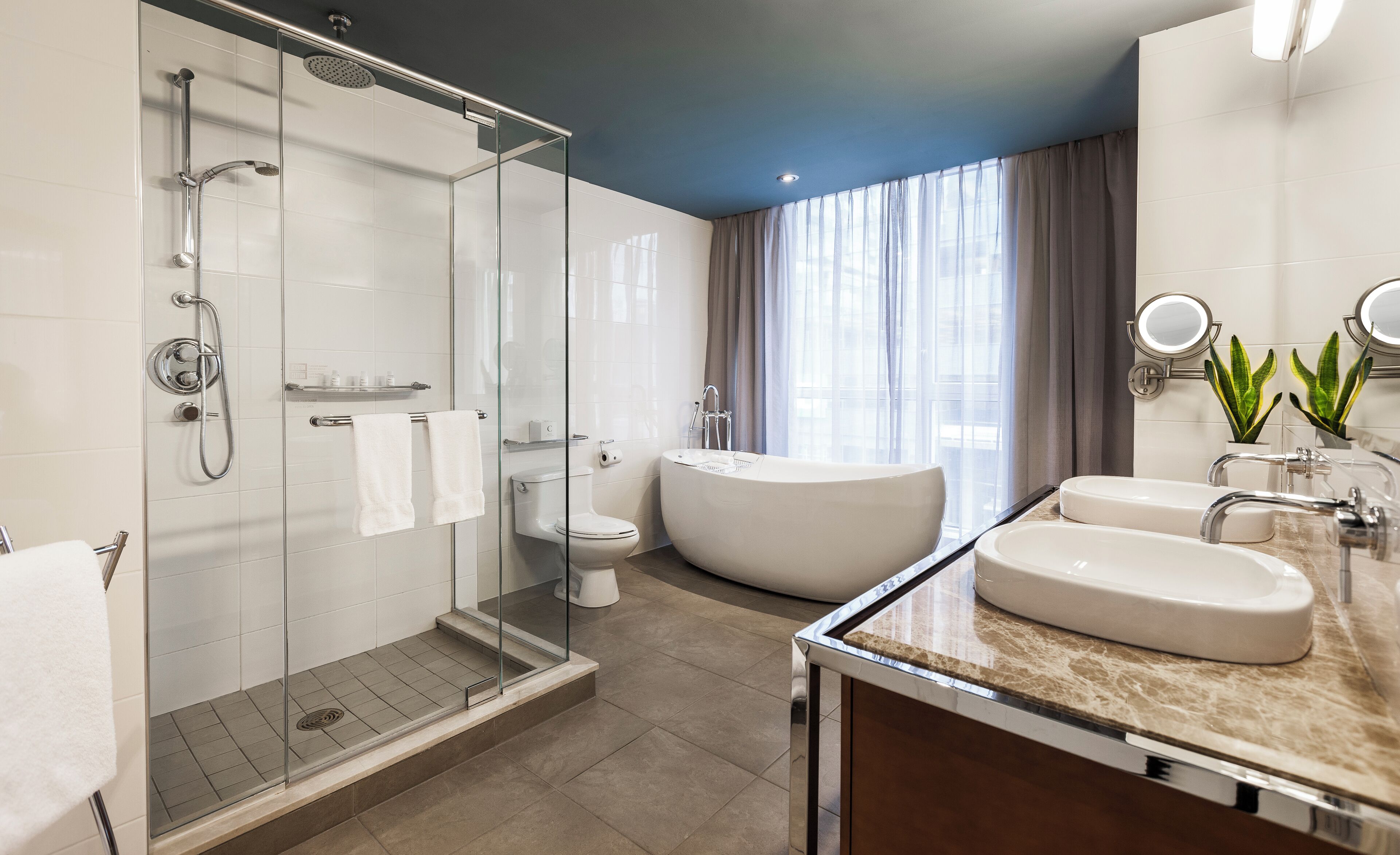 Un baño moderno con ducha de vidrio, bañera independiente y tocador con dos lavamanos.