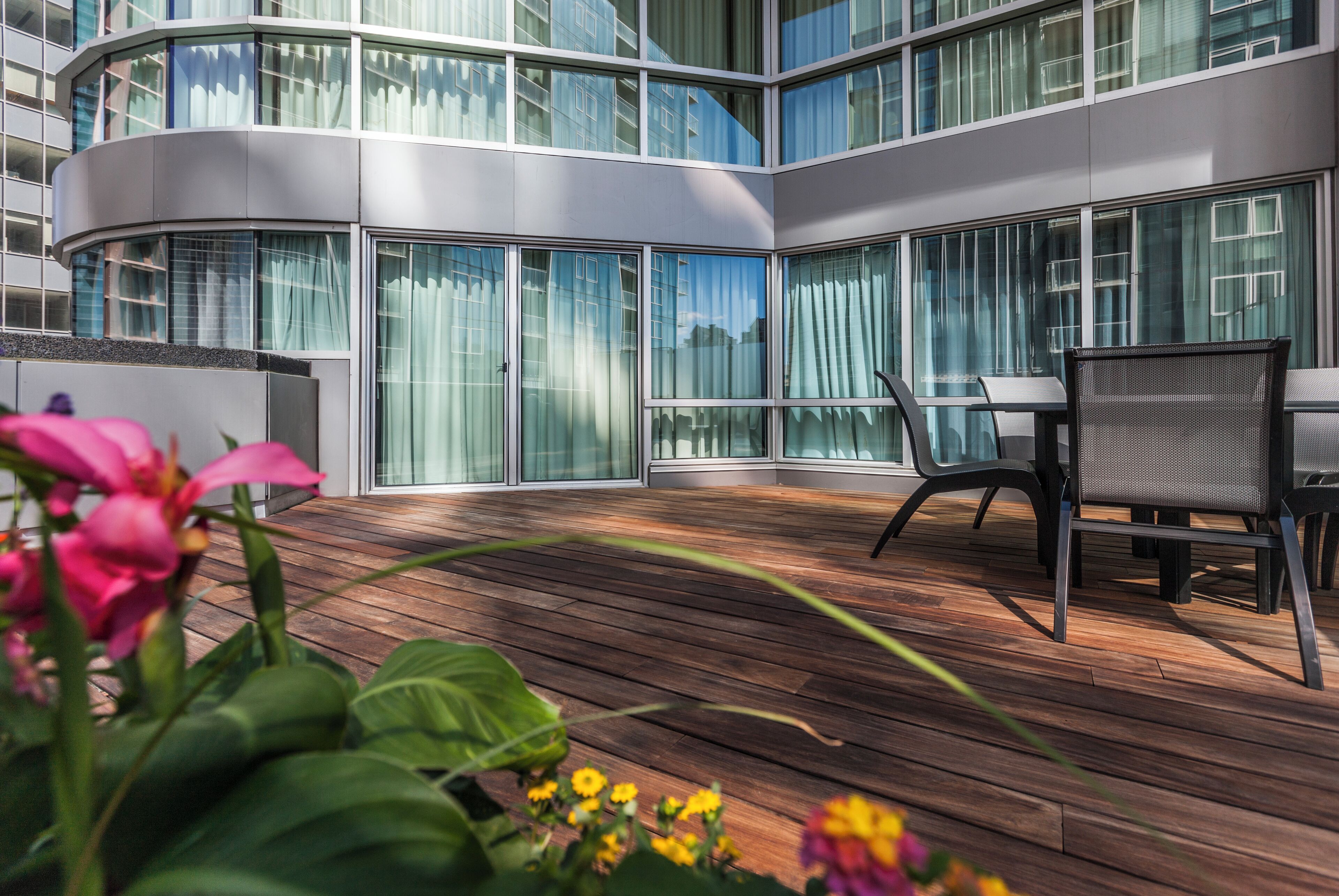 A modern outdoor patio with a curved balcony, wooden flooring, and outdoor furniture.