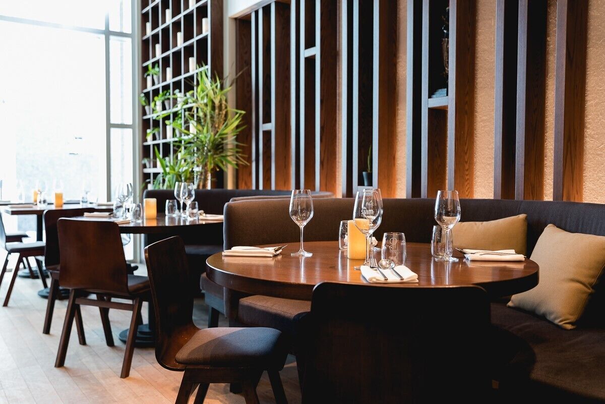 Een restaurant met ronde tafels, bruine leren zitplaatsen en een groot raam met uitzicht.