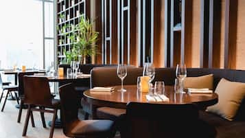 Een restaurant met ronde tafels, bruine leren zitplaatsen en een groot raam met uitzicht.