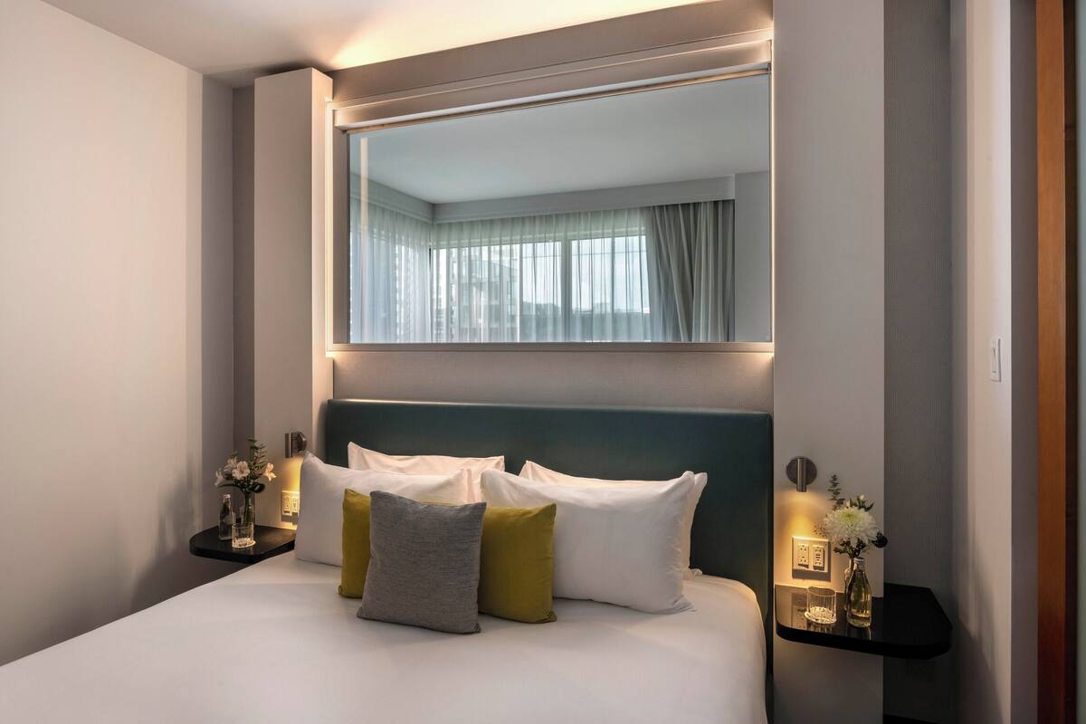 Una habitación de hotel con una cama grande, una mesita de noche con un florero y un espejo sobre la cama.