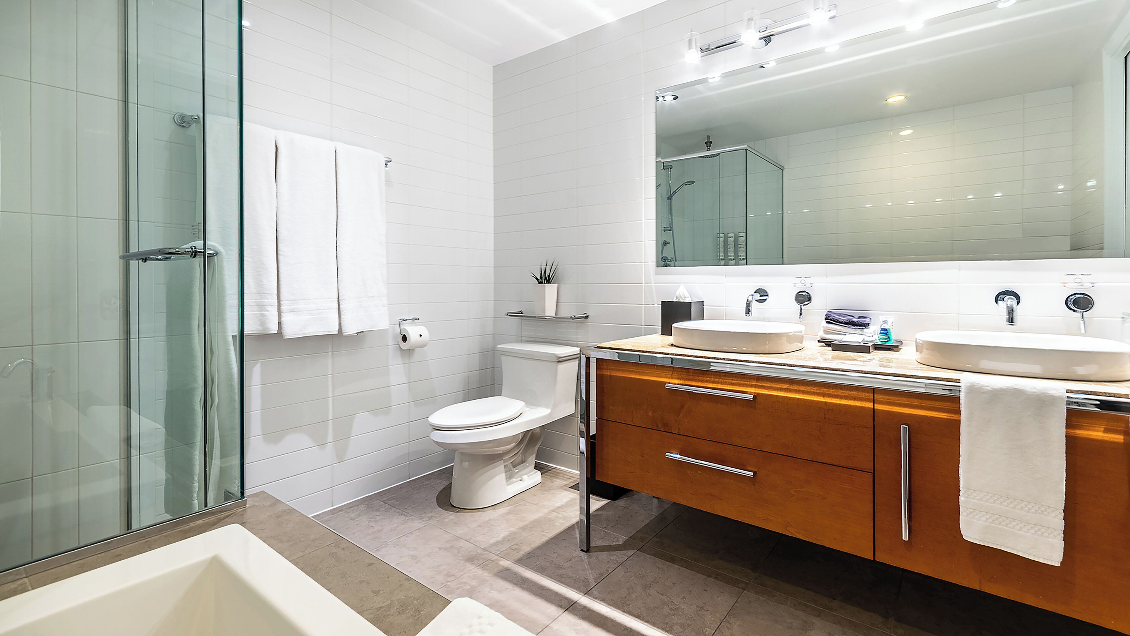 Une salle de bain moderne avec une douche à parois de verre, des toilettes, un lavabo avec un miroir et un meuble-lavabo avec des tiroirs.