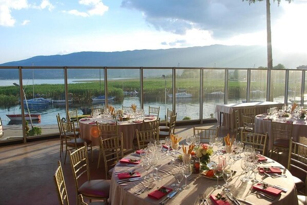 A restaurant with tables set for dining, overlooking a body of water with boats and greenery. - Hotel Drim (Struga)