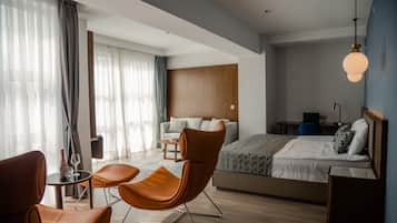 A modern hotel room with a bed, two brown leather chairs, a small table, and a desk with a lamp.