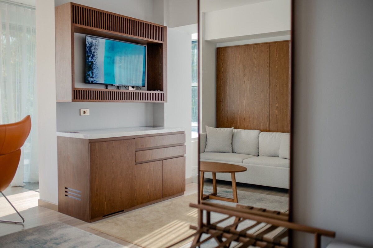 A modern living room with a wooden cabinet, a flat-screen TV, a white sofa, and a small wooden table.