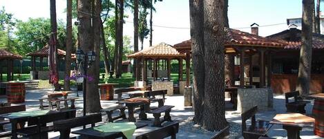 Outdoor seating with tables and benches, surrounded by trees.