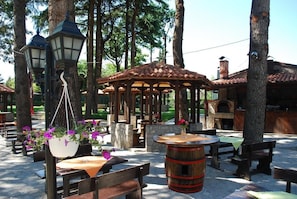 An outdoor seating area with wooden tables and benches, a gazebo, and a stone fireplace. - Hotel Drim (Struga)