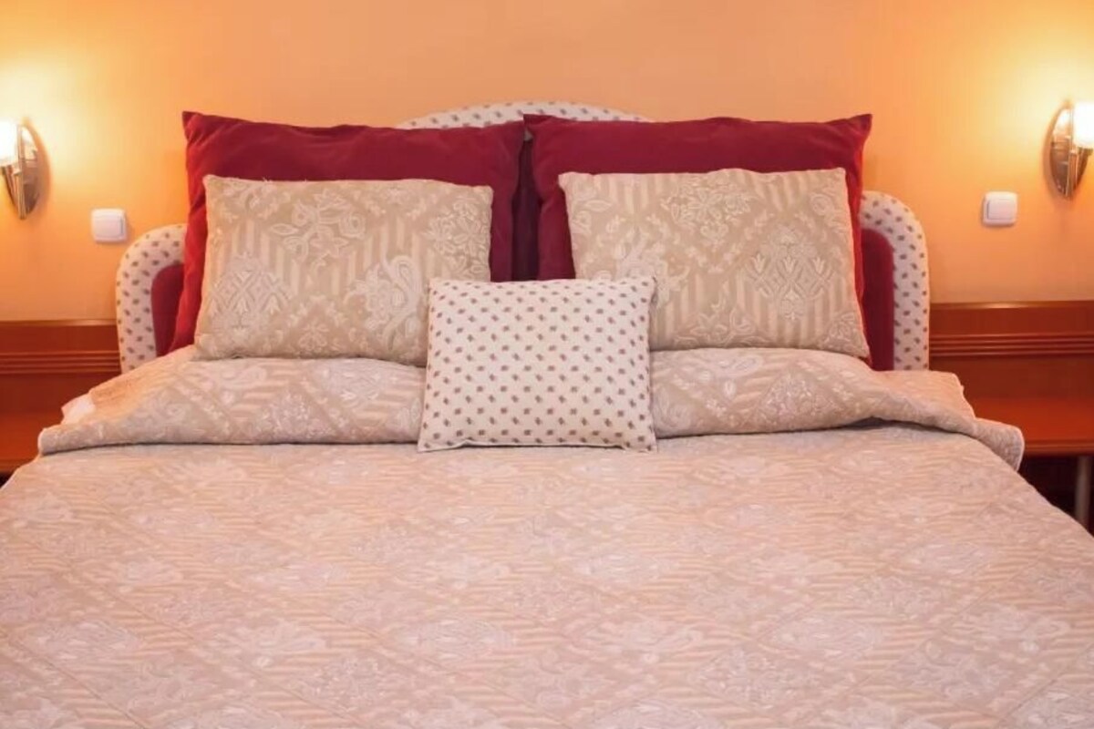 A bed with a patterned bedspread, two pillows with different designs, and two wall-mounted light fixtures.