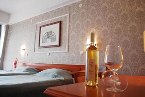 A hotel room with a bed, a table with a bottle and glass, a framed picture on the wall, and patterned wallpaper. - Hotel Drim (Struga)