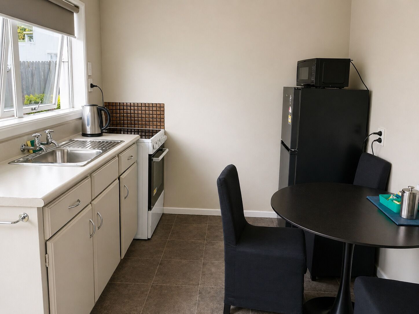 A compact kitchen with a sink, stove, and microwave, a dining table with chairs, and a window with a view of greenery.