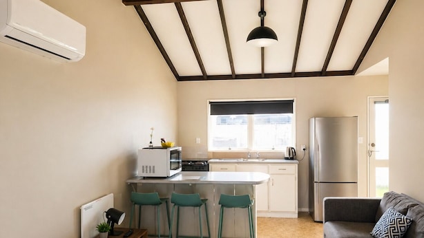Cocina compacta con microondas integrado, estufa y refrigerador. Hay un taburete de bar y un sofá en la sala.