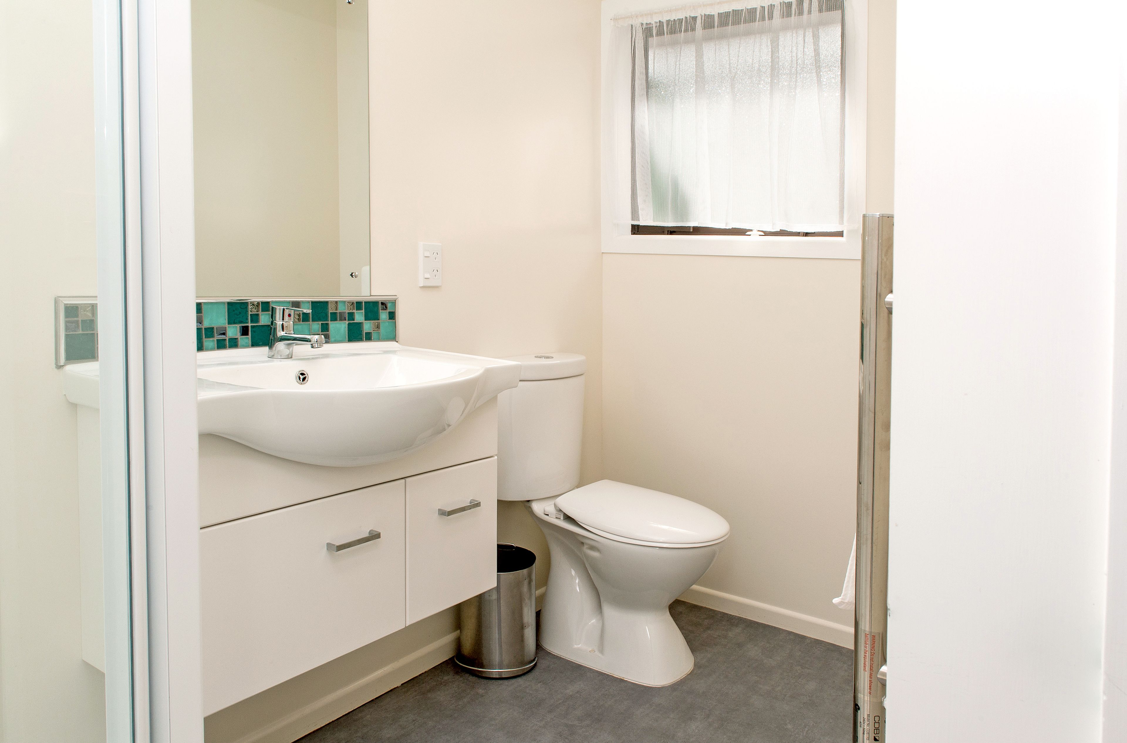 A bathroom with a white sink, toilet, and a trash can.