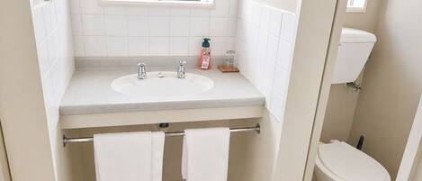 Une salle de bain avec un lavabo, deux robinets, une fenêtre, des toilettes et deux serviettes suspendues à un porte-serviettes.