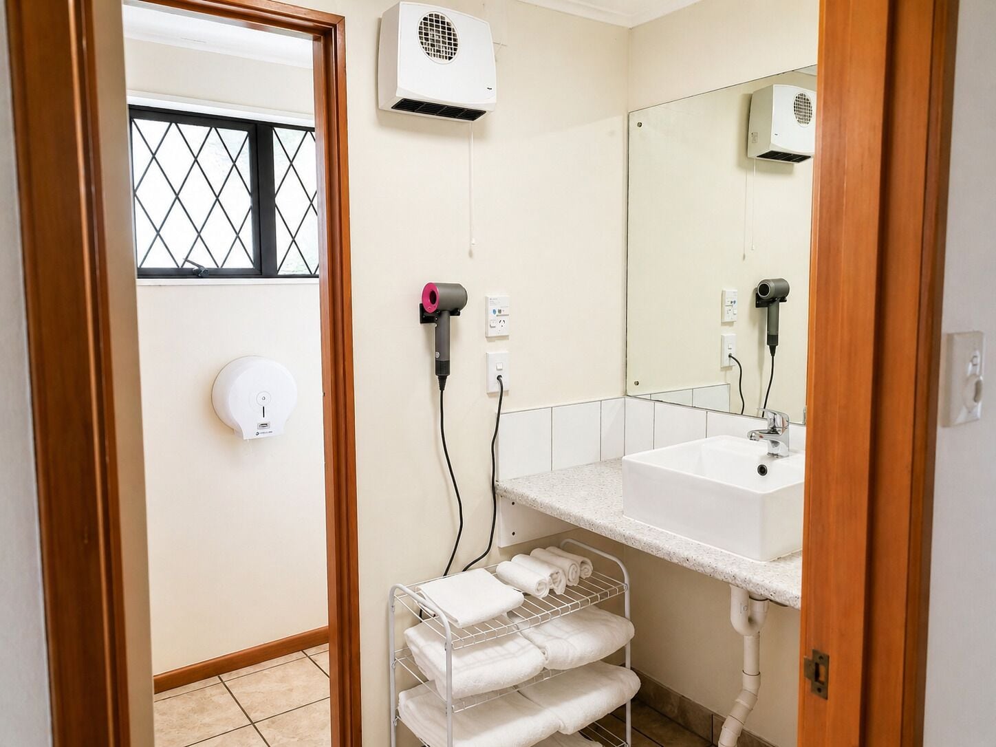 A bathroom with a sink, mirror, towel rack, and two hair dryers plugged in.