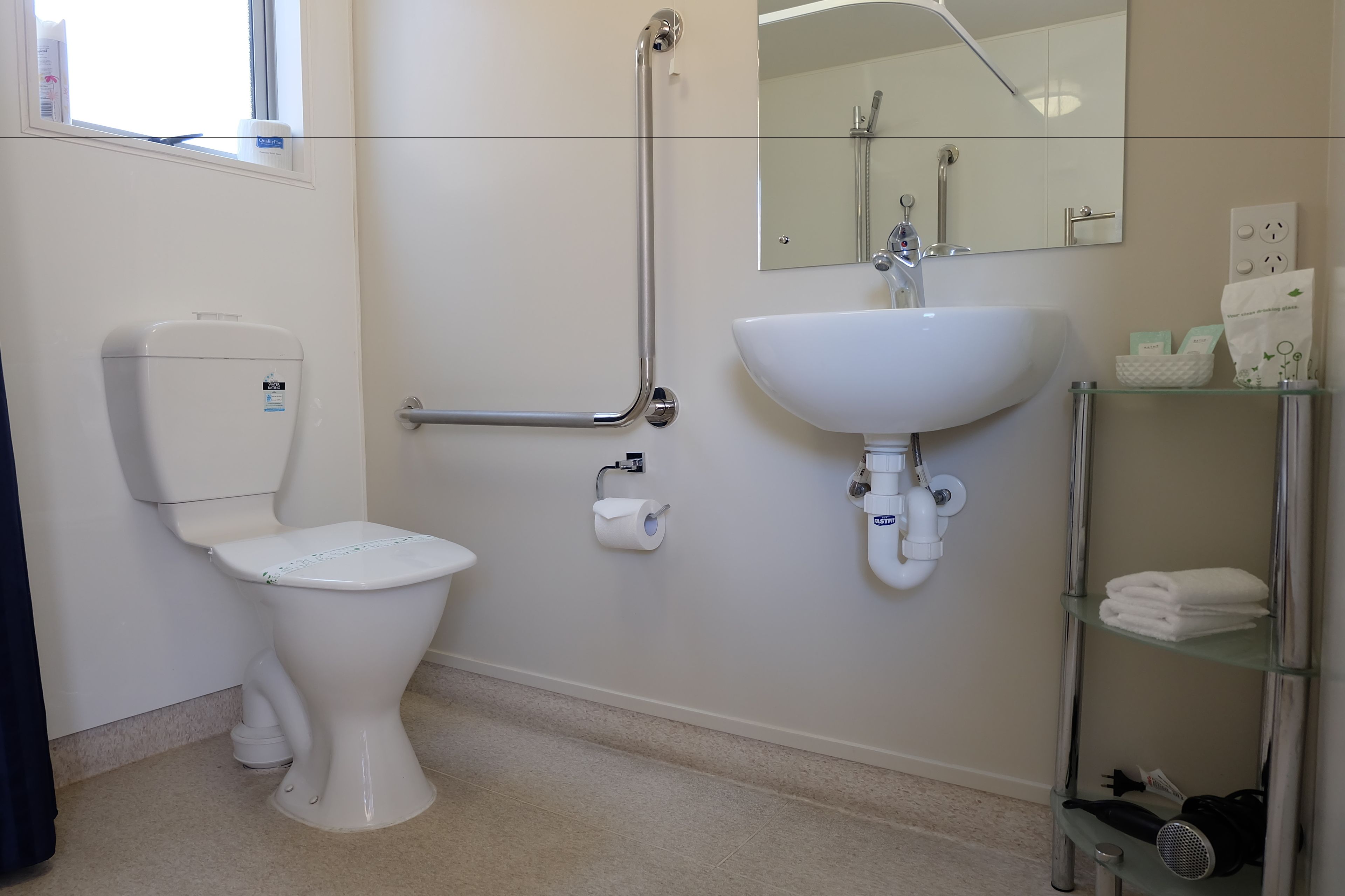 A modern bathroom with a toilet, bidet, sink, and glass shelves.