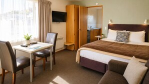 A hotel room with a bed, a desk with a chair, a TV, a wardrobe, and a small table with a plant.