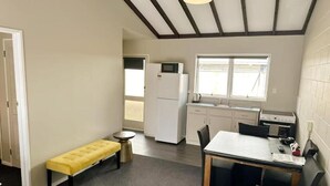 Habitación compacta con una banca, una mesa, kitchenette y una puerta que da a otra habitación.