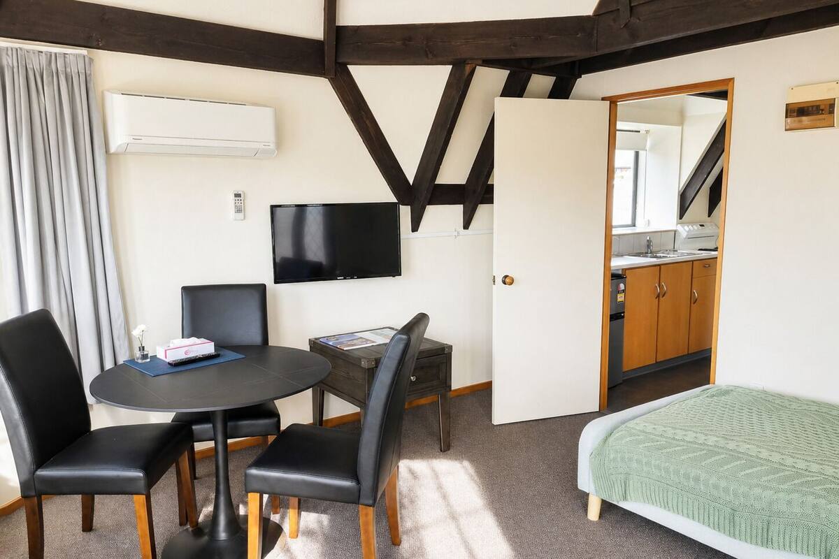 A room with a bed, a desk, a chair, a TV, and a kitchenette.