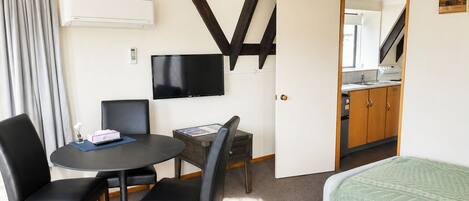 Een kamer met een bed, een bureau, een stoel, een televisie en een kitchenette.