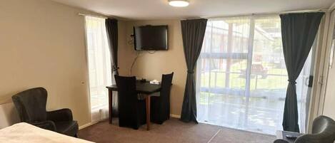 Quarto de hotel com cama, escrivaninha, cadeira, televisão e vista para o exterior.