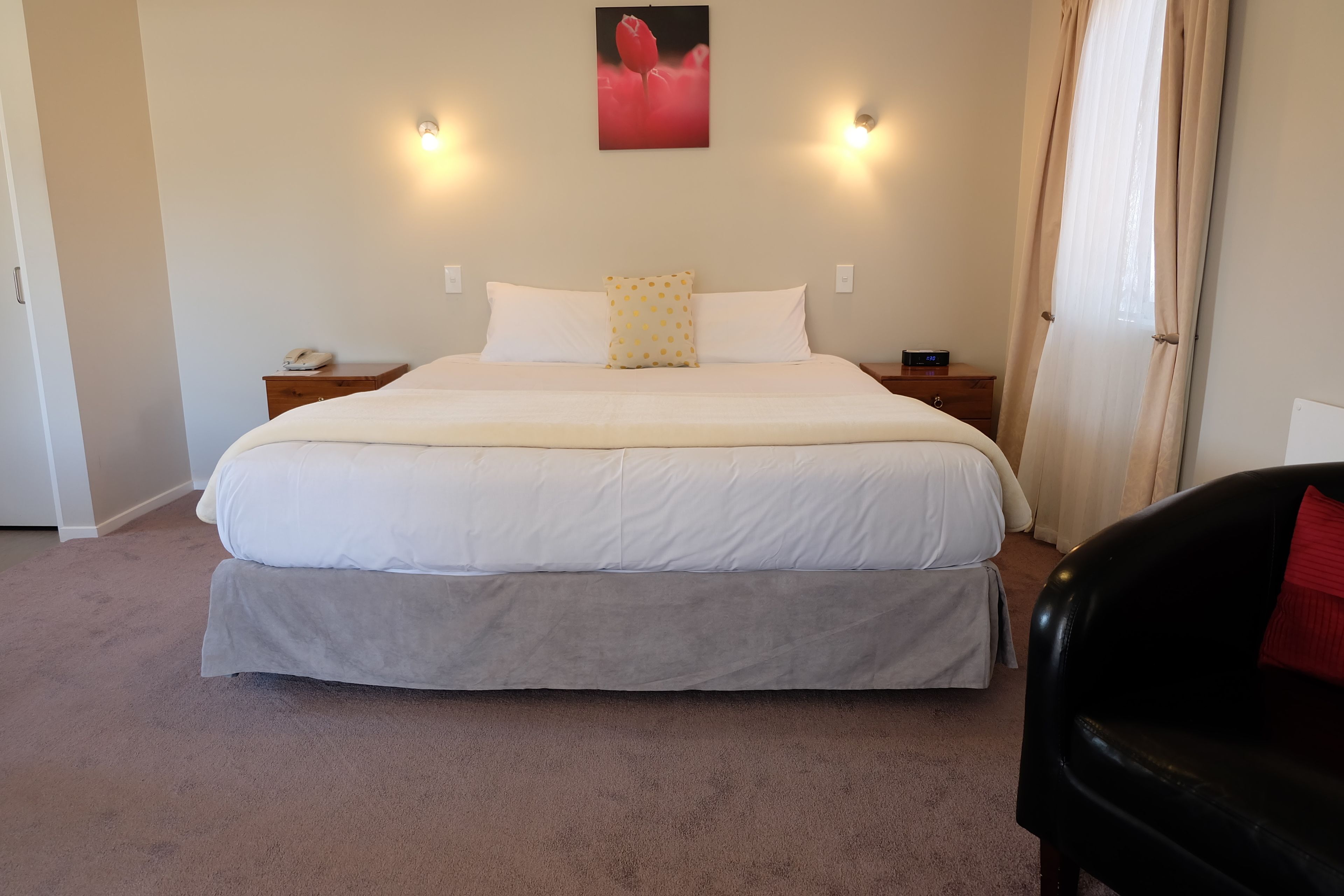 A bedroom with a large bed, two bedside tables, a nightstand, a telephone, and a window with curtains.