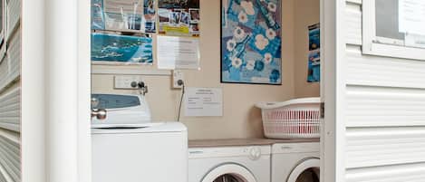 A laundry room with a washing machine, dryer, and a bulletin board with travel posters.