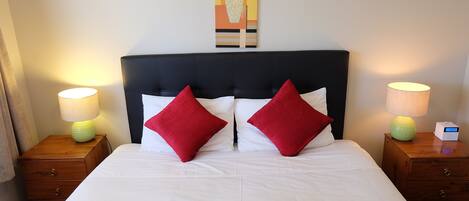 A neatly made bed with white bedding and two red pillows, flanked by wooden nightstands with lamps.