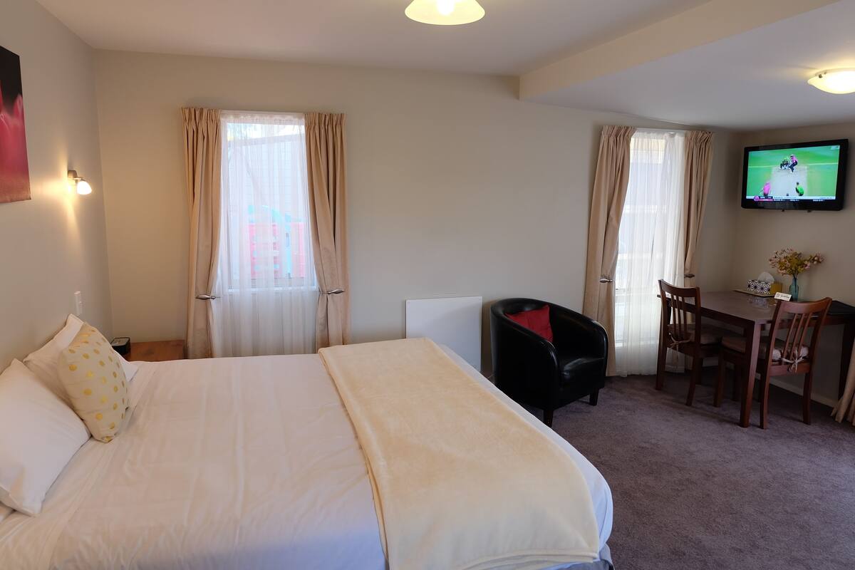 A hotel room with a large bed, a desk, a chair, and a TV on the wall.