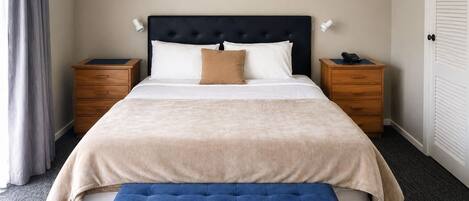 A neatly made bed with a headboard, two bedside tables, a bench, and a door.