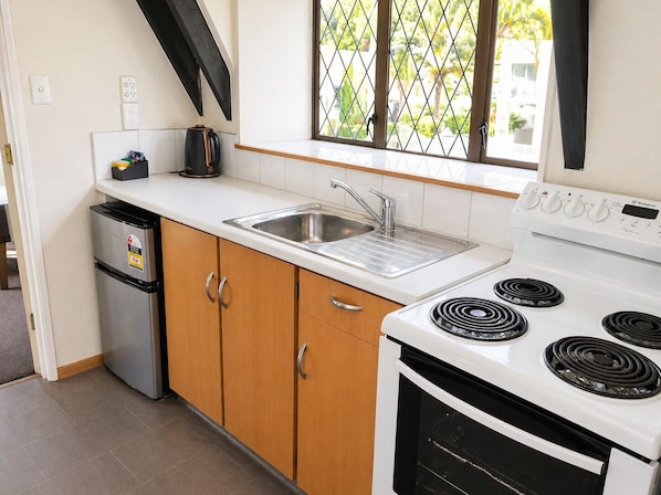 A kitchen with a stove, sink, and a small refrigerator.