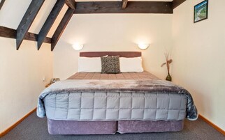 Un dormitorio con cama, cabecera, lámparas de noche y un jarrón con ramas.