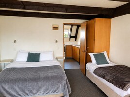 A room with two beds, a wooden wardrobe, a small kitchenette, and a door leading to another room.
